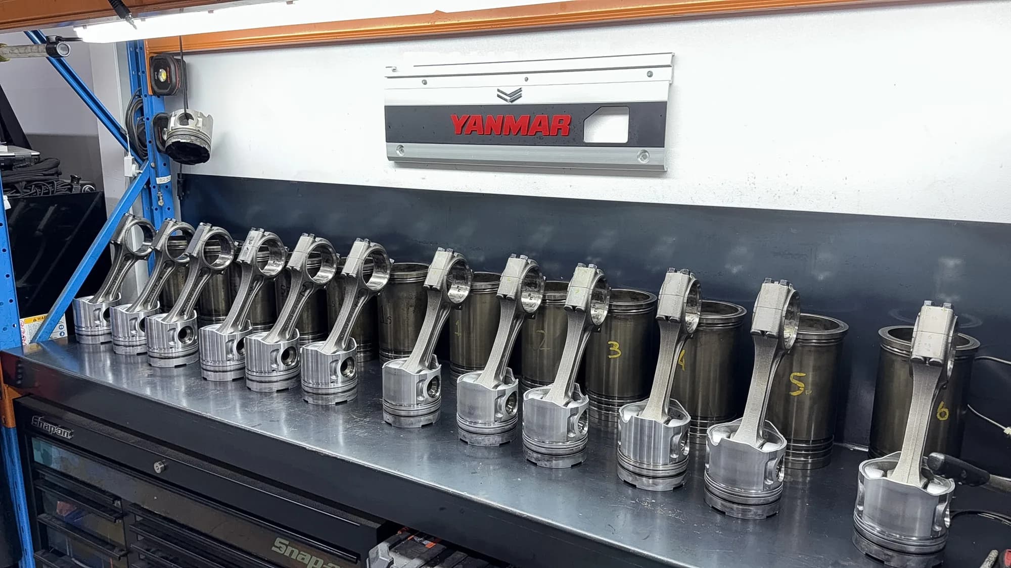 Pistons, connecting rods and cylinder liners lined up on the bench beneath a Yanmar sign