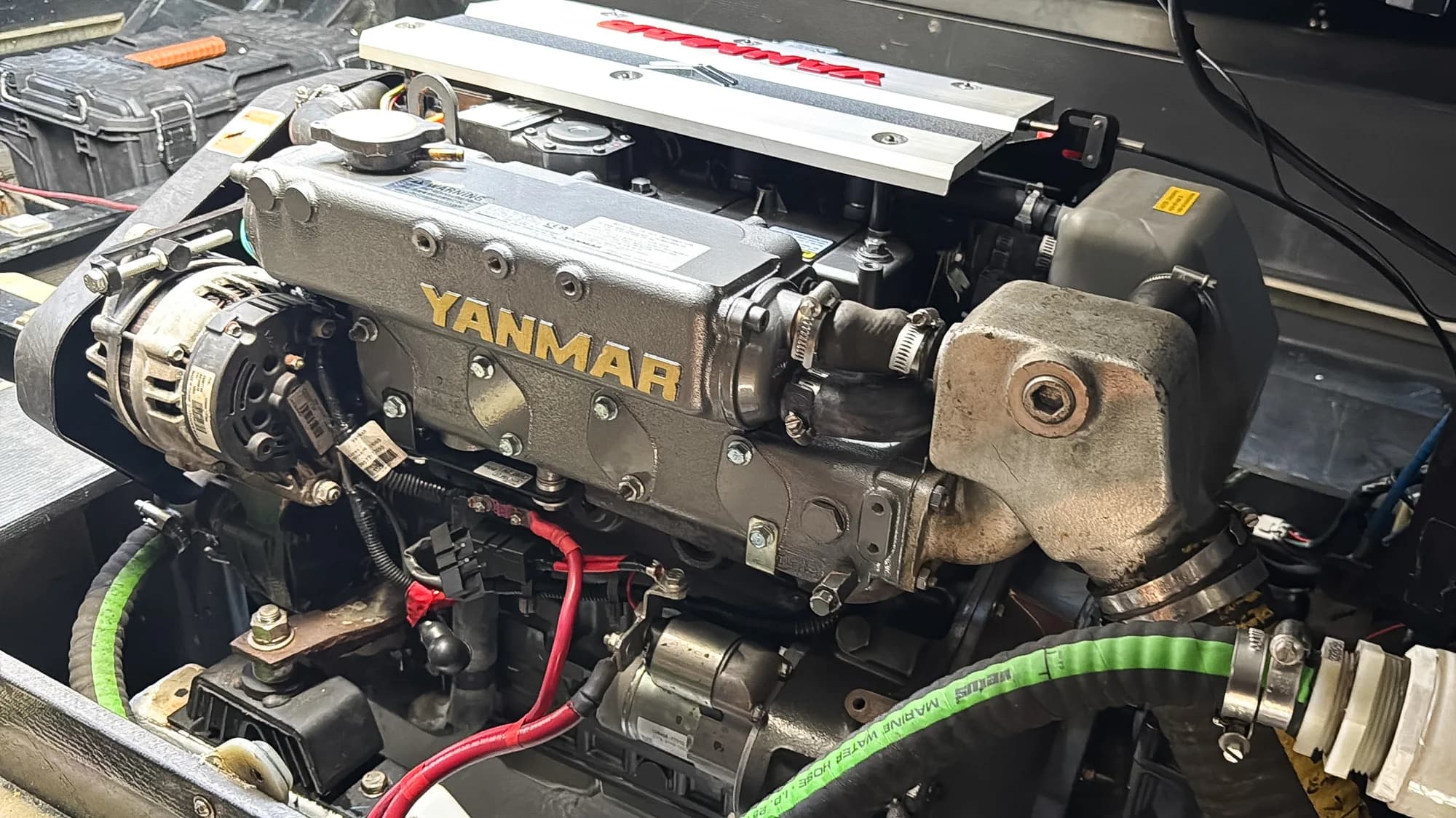 A Yanmar marine diesel installed in an engine bay, with the alternator and marine water hose in view